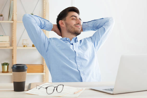 istock Relaxed man in blue shirt having rest during work in office, resting head on palms, spreading elbows, smiling, looking satisfied 1217002346