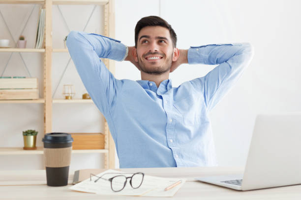 istock Young positive office man having rest in office, spreading elbows, stretching his back, taking break from work tasks and projects, smiling happily, looking to left 1217002373