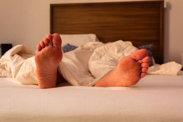 istock Feet on a white bed covered with white bed sheets, concept of sleep, rest and relaxation 1217006333