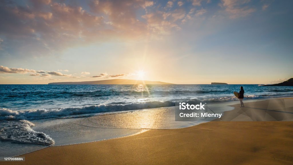 Surfer at the Beach Maui Island Sunset Panorama Hawaii USA Lonely surfer standing at the beach with her surfboard enjoying the sunset light over the pacific ocean waves at Makena Beach. Maui Island, Hawaii Islands, Polynesia, USA. Hasselblad 50MP Panorama Crop. Surfing Stock Photo