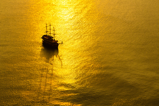 Vintage ship sailing in the calm golden sea at sunset, aerial view.