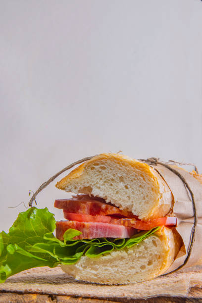 Sandwich with meat tomato and salad in a paper wrapper. Sandwich with meat tomato and salad in a paper wrapper, on a light background тост stock pictures, royalty-free photos & images