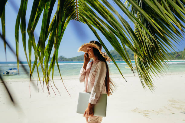 istock Woman talking on phone with laptop on beach 1217010560