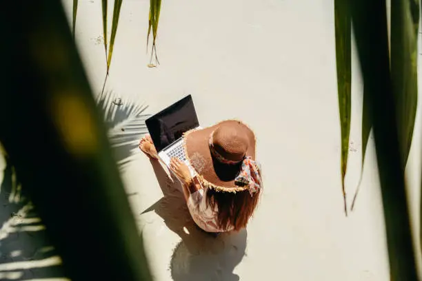 Woman freelancer on the beach. Working remotely on the laptop computer through the internet. Working while travelling. Top view.