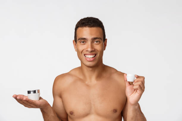 foto di un uomo afro-americano a torso libero che sorride e tiene la crema isolata su sfondo bianco - hairy men shaving chest foto e immagini stock