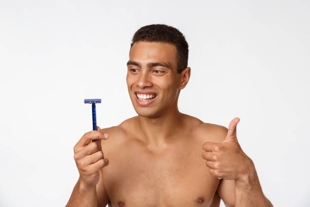 primo piano di un uomo africano nudo felice che tiene il rasoio isolato su sfondo grigio. - hairy men shaving chest foto e immagini stock