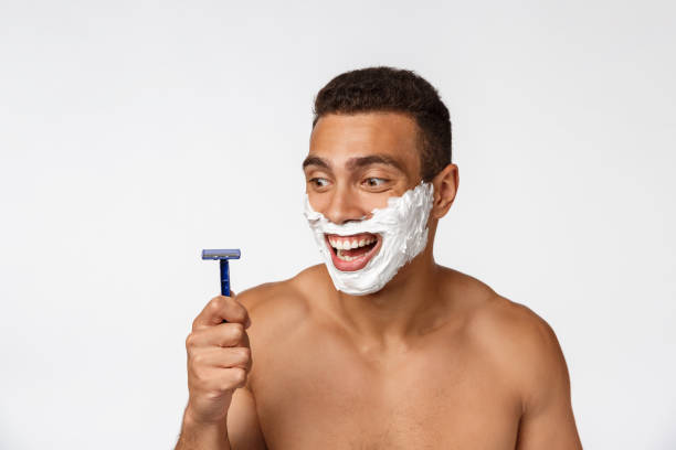 primo piano di un felice uomo africano nudo con il viso in schiuma da barba che tiene il rasoio isolato su sfondo grigio. - hairy men shaving chest foto e immagini stock