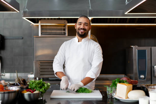 jeune chef africain beau restant dans la cuisine professionnelle dans le restaurant préparant un repas de viande et de légumes de fromage. - beautiful smiling vegetable calcium photos et images de collection