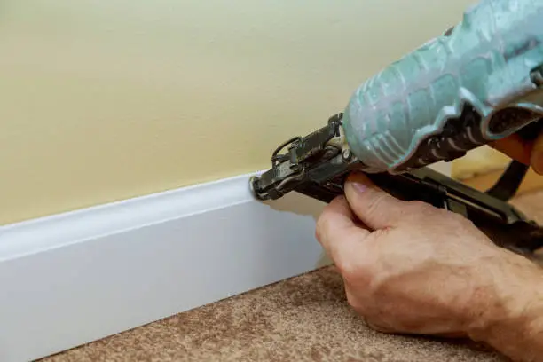 Carpenter brad using air nail gun to base moulding trim, with room renovation new house finishing