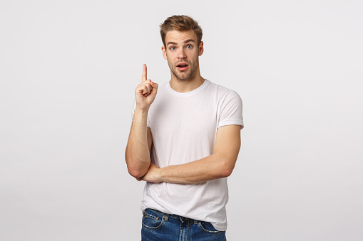 Excited attractive blond man with bristle, have suggestion, raise index finger eureka gesture, asking question or speaking, have idea, sharing plan, want someone hear him out, stand white background.