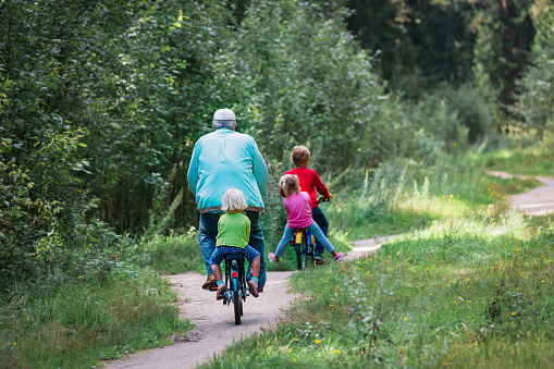 active senior with grandkids riding bikes in nature, family exercise outdoors