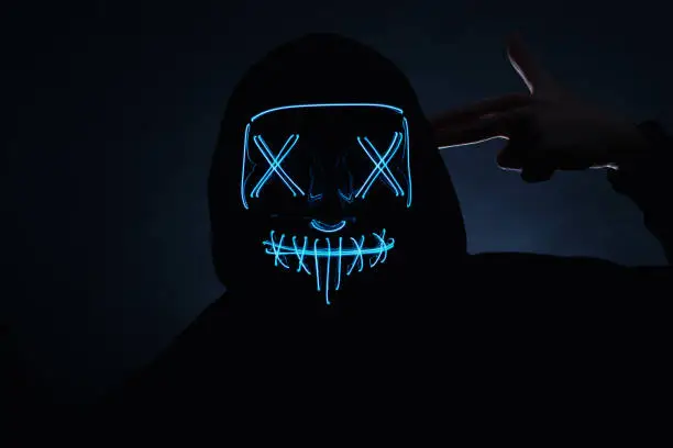 Portrait of a man hiding his face behind a glowing neon mask. Night club, Halloween party