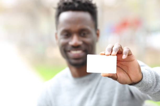 glücklicher schwarzer mann zeigt leere kreditkarte im park - template business business card holding stock-fotos und bilder