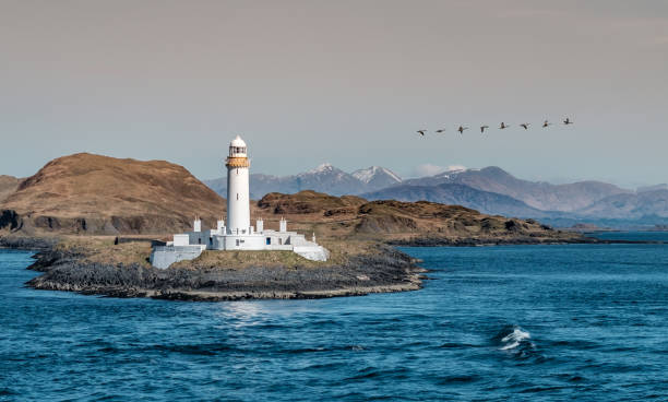 Old lighthouse in Scotland, with snowcapped highland peaks in the background Old lighthouse in Scotland, with snowcapped highland peaks in the background oban stock pictures, royalty-free photos & images