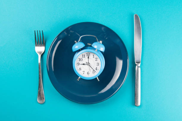 istock Alarm clock with fork and knife on the blue plate on blue table. Time to eat, Breakfast, Lunch Time and Dinner concept 1217020440