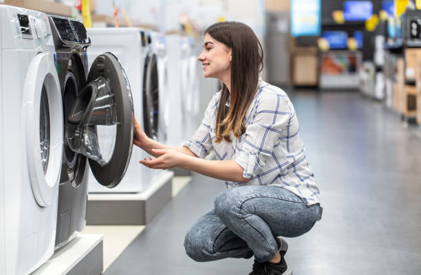 eine junge frau in einem geschäft wählt eine waschmaschine. - haushaltsmaschinen stock-fotos und bilder