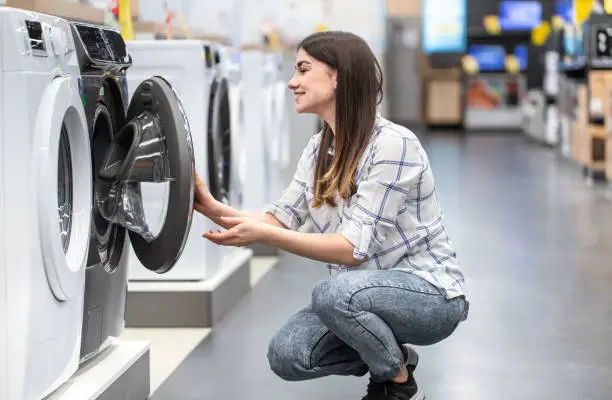 Photo of A young woman in a store chooses a washing machine.