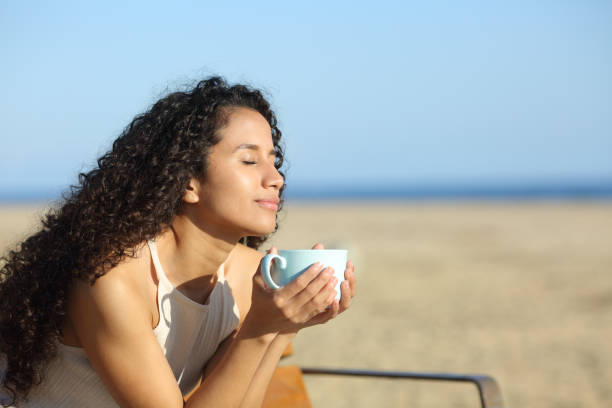 femme latine appréciant une tasse de café sur la plage - at the beach photos et images de collection