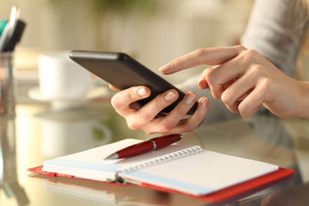 Woman checking phone with agenda over the table Close up of woman hands checking smart phone with personal organizer diary or agenda over the table at home online calendar stock pictures, royalty-free photos & images