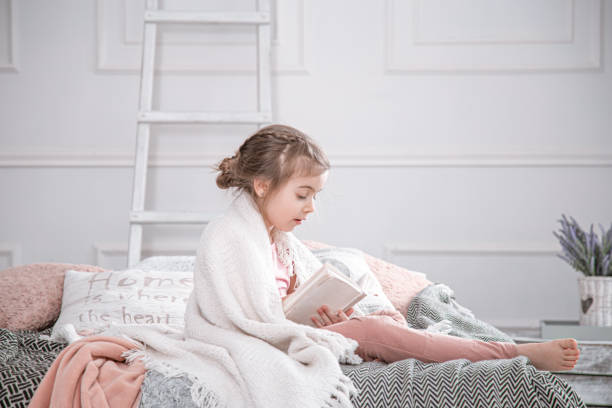 istock Cute little girl reading a book on the bed. 1217023215
