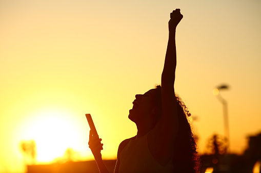 Silhouette of excited woman holding phone celebrating