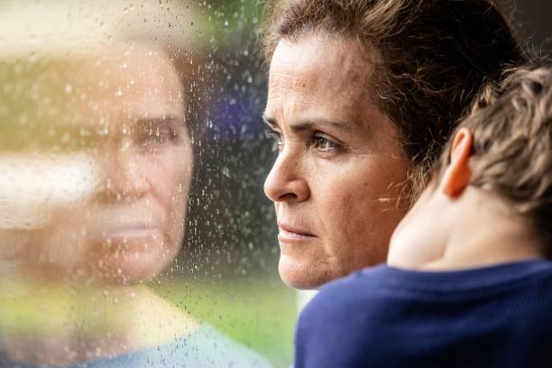 mature woman posing with her son, very sad looking through window worried about covid-19 lockdown - unemployment fear depression women imagens e fotografias de stock