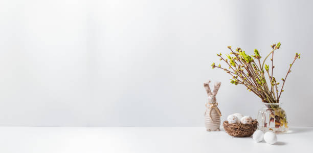 istock Home interior with easter decor. Green buds on branches in a glass vase, easter eggs on a light background 1217025132