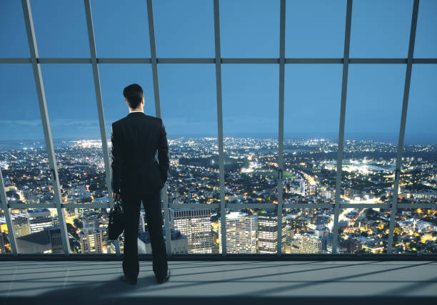 istock Businessman with case standing in night office 1217026335