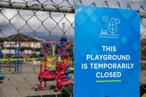 This Playground Is Temporarily Closed Sign with playground taped off in background
