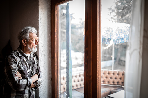Sad Mature man Suffering From Agoraphobia Looking Out Of Window