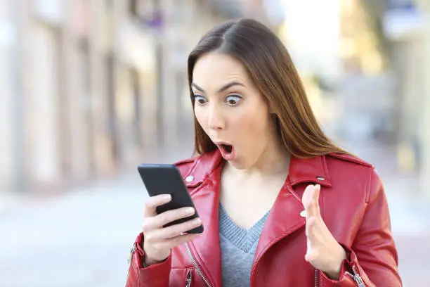 Surprised woman with eyes and mouth open wearing a red jacket looking at her phone screen