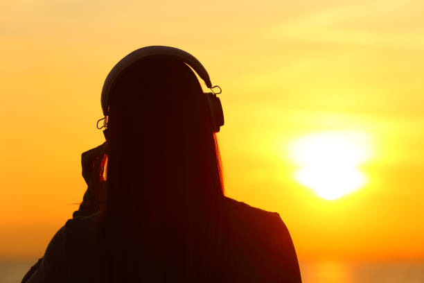 mulher usando fones de ouvido ouvindo música ao pôr do sol - romantic sky audio - fotografias e filmes do acervo