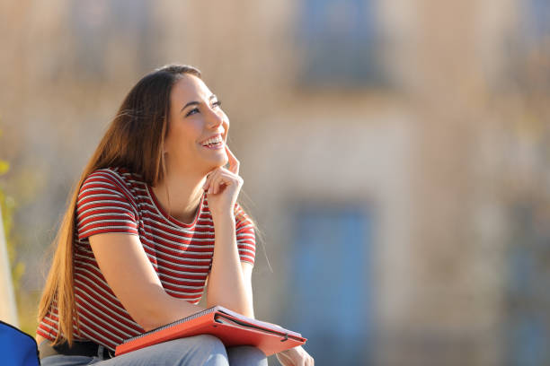 Happy student thinking looking at side in a campus Happy student thinking looking at side sitting outdoors in a university campus women satisfaction decisions cheerful stock pictures, royalty-free photos & images