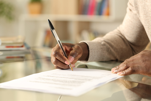 Hombre negro manos firmando documento en un escritorio en casa photo