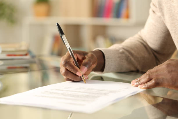 hombre negro manos firmando documento en un escritorio en casa - llenar el formulario fotografías e imágenes de stock