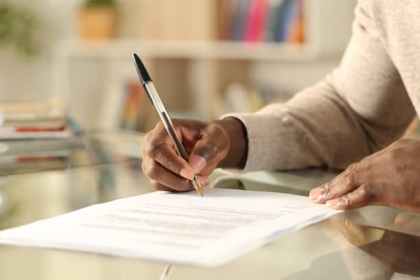 black man hands signing document on a desk at home - endorsing business application form filling imagens e fotografias de stock