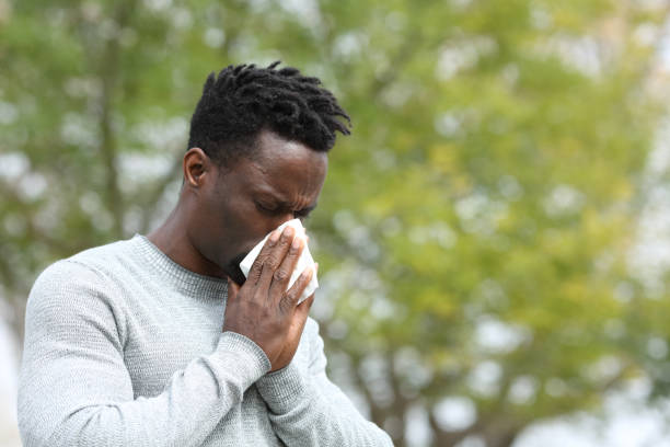 Allergic black man blowing on wipe in a park on spring season Allergic black man blowing on wipe in a park on spring season a sunny day sneezing photos stock pictures, royalty-free photos & images