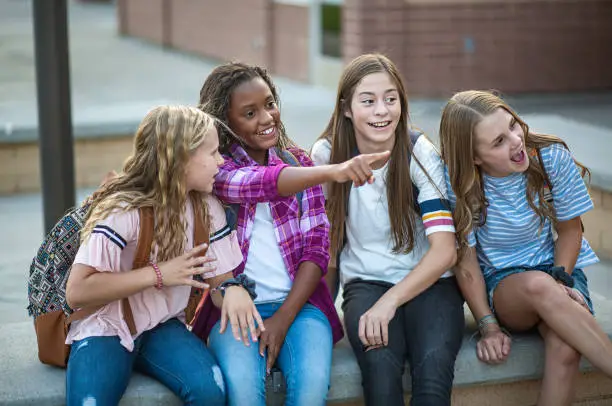 Candid photo of a group of teenage girls socializing, laughing and talking together at school. A multi-ethnic group of real junior high aged students