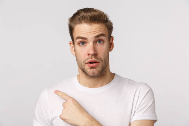 istock Curious guy consulting with shop assistant as pointing finger left at product. Attractive blond bearded man in white t-shirt looking interested, asking question, standing white background 1217034146