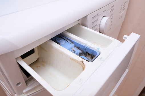 Dirty moldy washing machine detergent and fabric conditioner dispenser drawer compartment close up. Mold, rust and limescale in washing machine tray. Home appliances periodic maintenance concept.