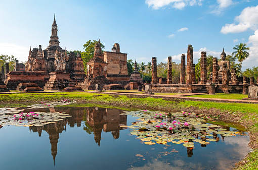 The Wat Mahathat temple reflecting in a pond with lotus flowers, Sukhothai, Thailand.