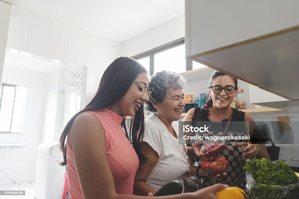 Abuela, madre e hija desempaquetando comestibles en la cocina - Foto de stock de Familia libre de derechos
