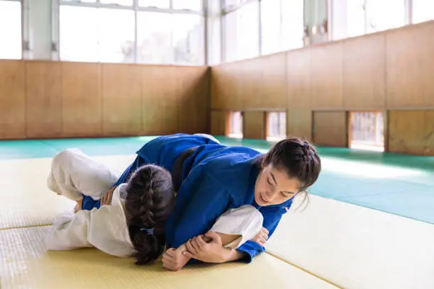 Young female athletes playing Judo in Dojo, performing 'Katame waza’ grappling technique