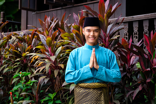A portrait of young malay man in his traditional teal cloth, samping songket and songkok. Selamat Hari Raya gesture.