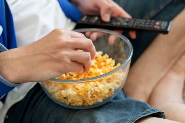 Coronavirus stay at home quarantine self isolation entertainment concept. Man sitting with the bowl of popcorn and holding a tv remote. Unealthy lifestyle. Coronavirus stay at home quarantine self isolation entertainment concept. Man sitting with the bowl of popcorn and holding a tv remote. Unealthy lifestyle. popcorn snack bowl isolated stock pictures, royalty-free photos & images