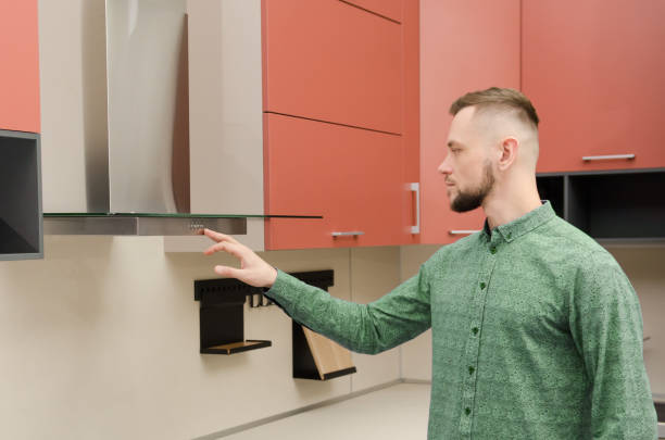 Attractive bearded man in a green shirt turns on a fume hood in a modern kitchen Attractive bearded man in a green shirt turns on a fume hood in a modern kitchen. fume cupboard stock pictures, royalty-free photos & images