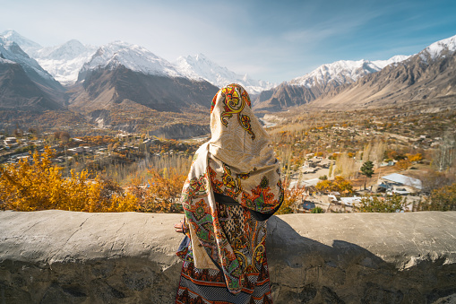 Una mujer con un vestido tradicional sentado en la pared y mirando al valle de Hunza en la temporada de otoño, Gilgit Baltistan en Pakistán photo