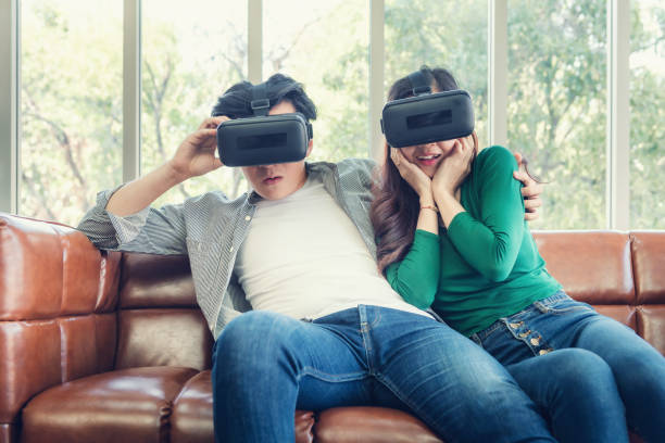 istock Young Couple Having Fun While Watching Video Via Virtual Reality Together. Couple Love Having Enjoyment With Electronic VR Goggles Gaming on Couch. Entertainment Innovation/Lifestyles Concept 1217081915