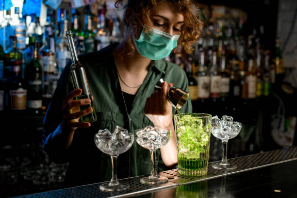 의료 용 마스크에 젊은 바텐더 소녀는 얼음 유리에 비커에서 녹색 액체를 부어. - bar 뉴스 사진 이미지