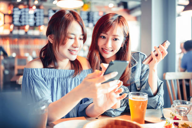 istock cheerful young friends looking at smart phone in restaurant 1217082784